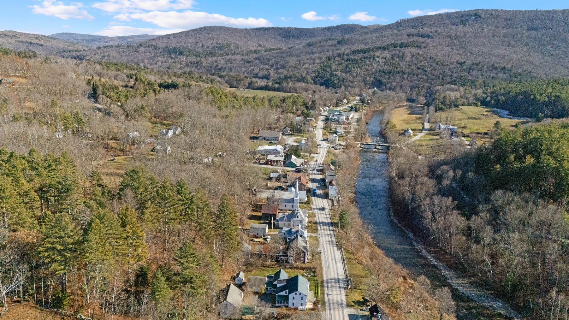 Aerial view of Bridgewater village in the Vermont valley, river winding past historic homes with mountains beyond