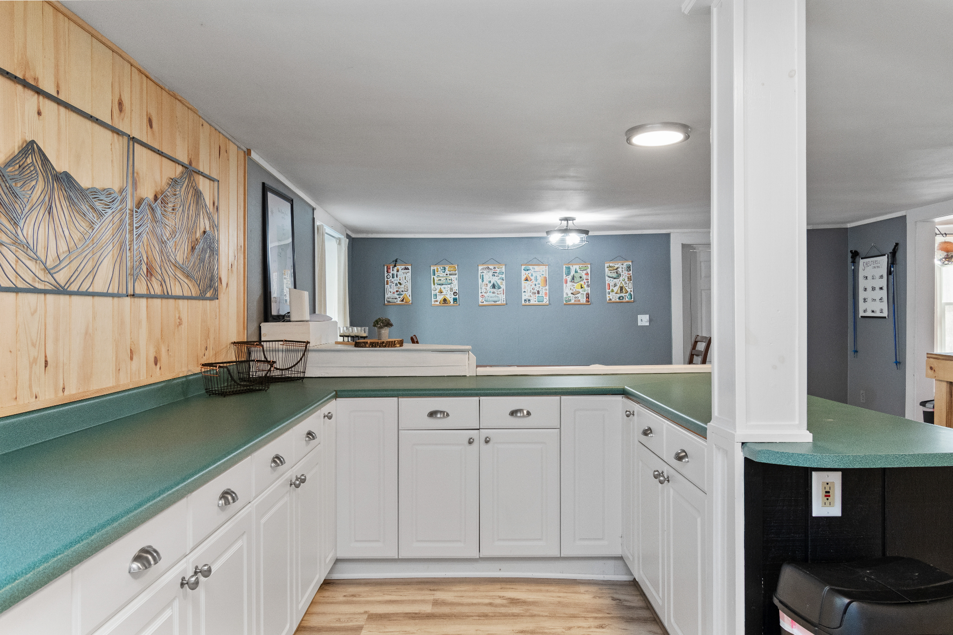 Main house kitchen with green countertops, white cabinets, and mountain art